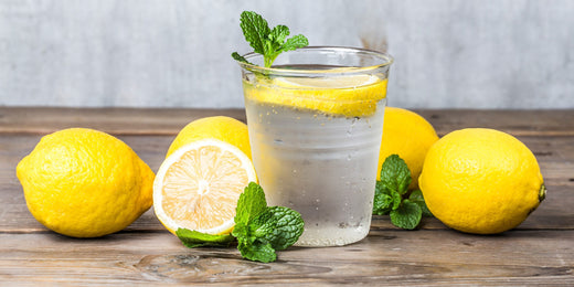 Lemon water in a glass cup on a table surrounded by squeezed lemon halves